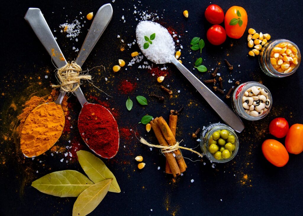 pexels-photo-4134514 Top view of dry turmeric and paprika near bay leaves with cinnamon sticks and sea salt in spoons near jars with popcorn grains and olives with ripe colorful cherry tomatoes